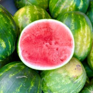 Half watermelon on top of a bunch of whole watermelons