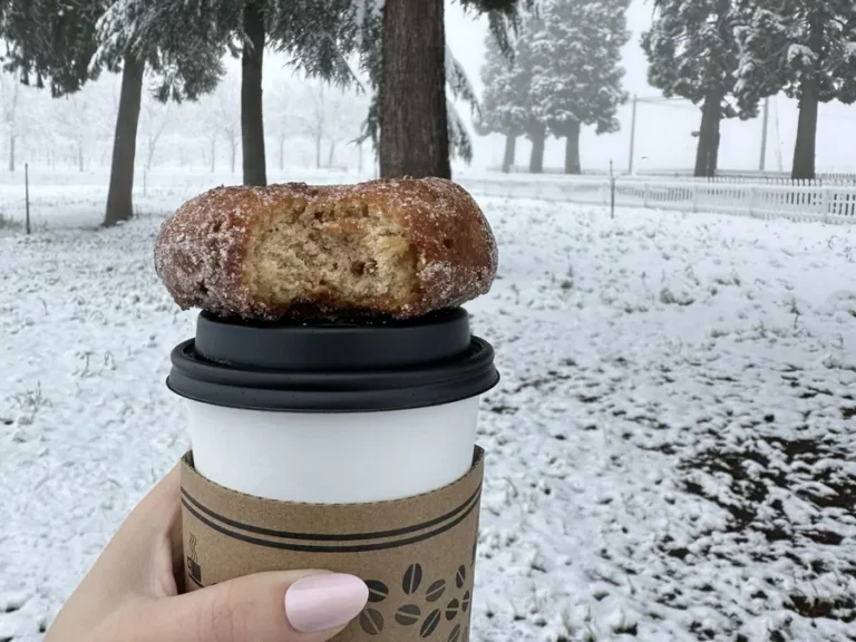 A coffee and donut with snow on the ground shows Apple Hill in winter